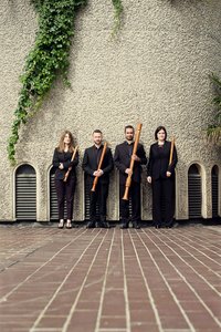 The Flautadors holding recorders standing against a concrete wall with ivy growing down